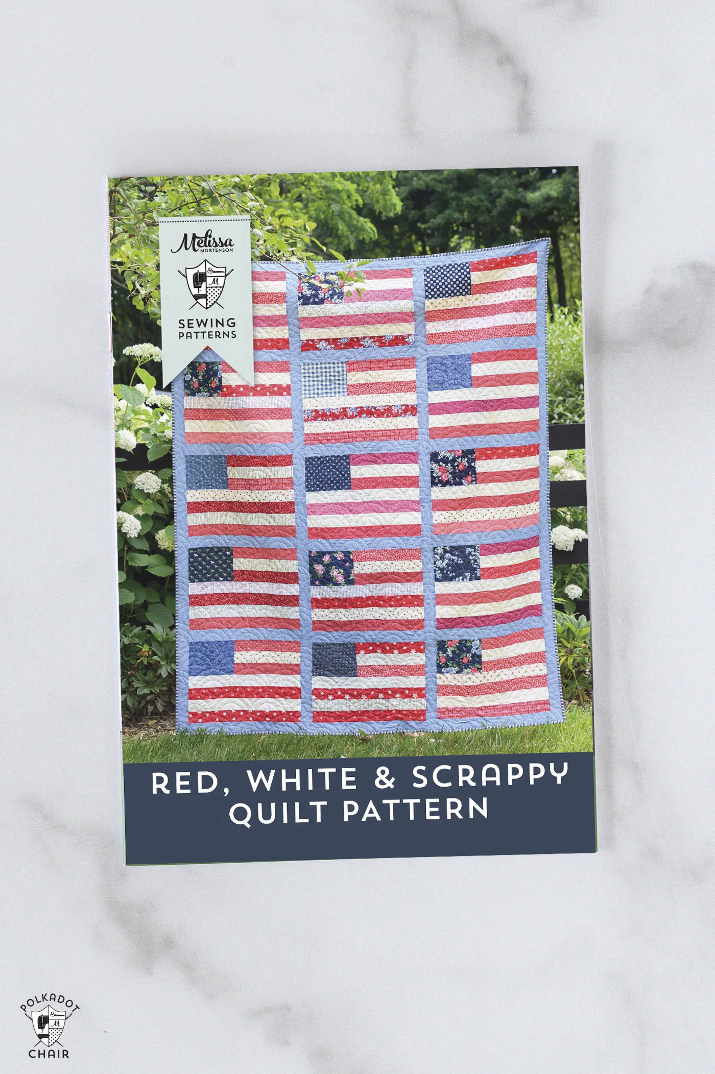 Quilt pattern book titled 'Red, White & Scrappy' with a quilt displayed outdoors.