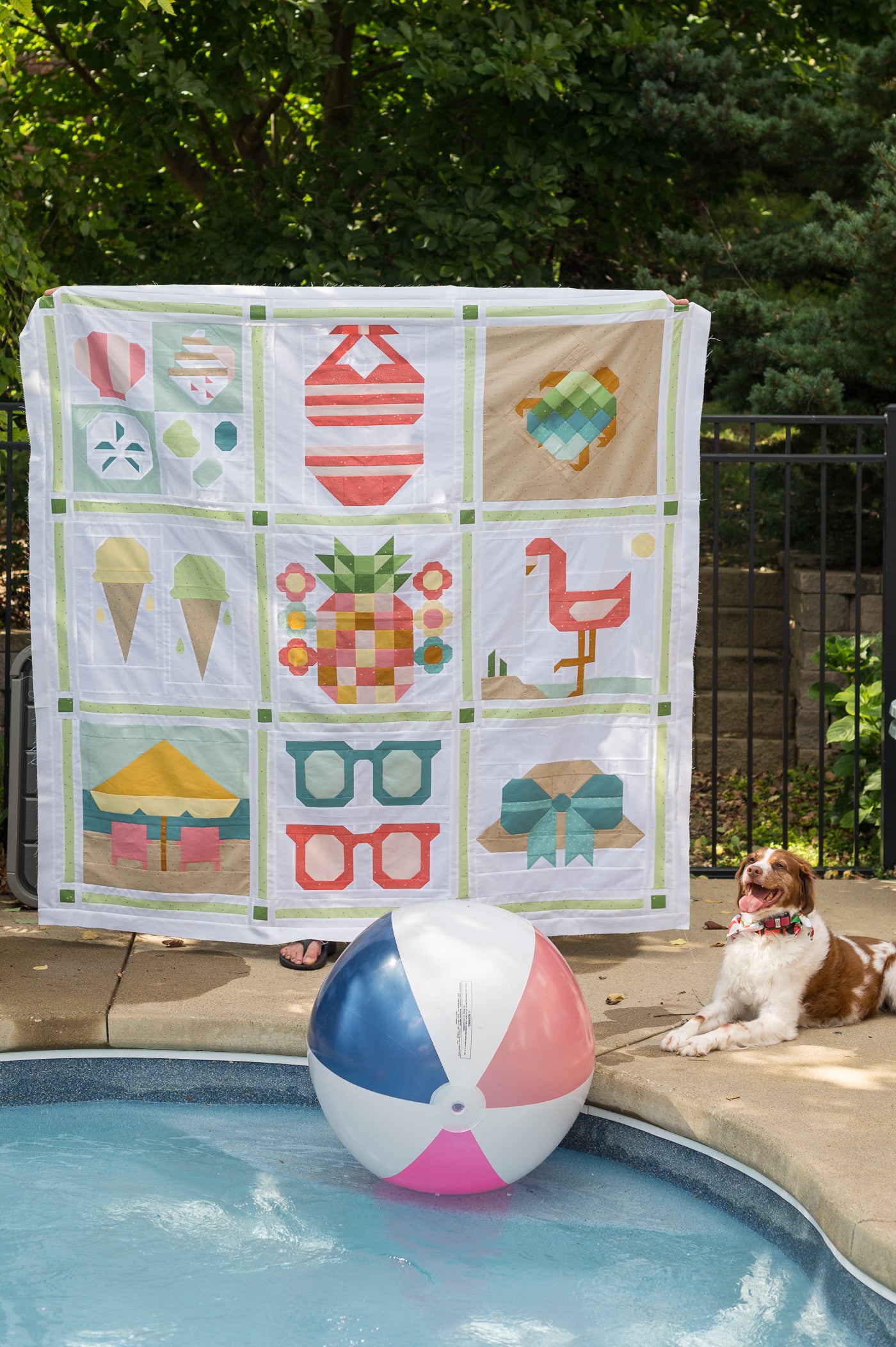 Colorful quilt with various patterns displayed by a poolside with a dog and beach ball.