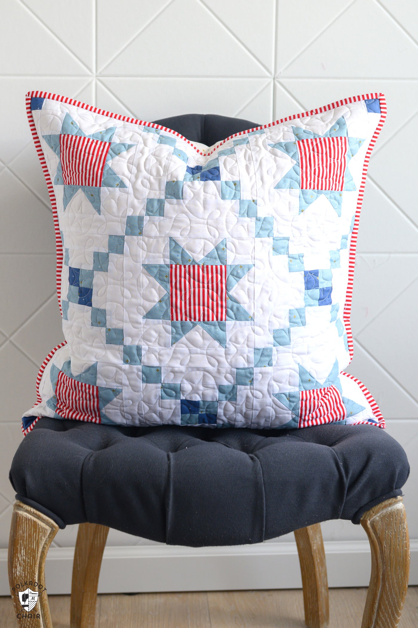 Patchwork pillow with red and blue patterns on a black cushioned chair against a white tiled wall.