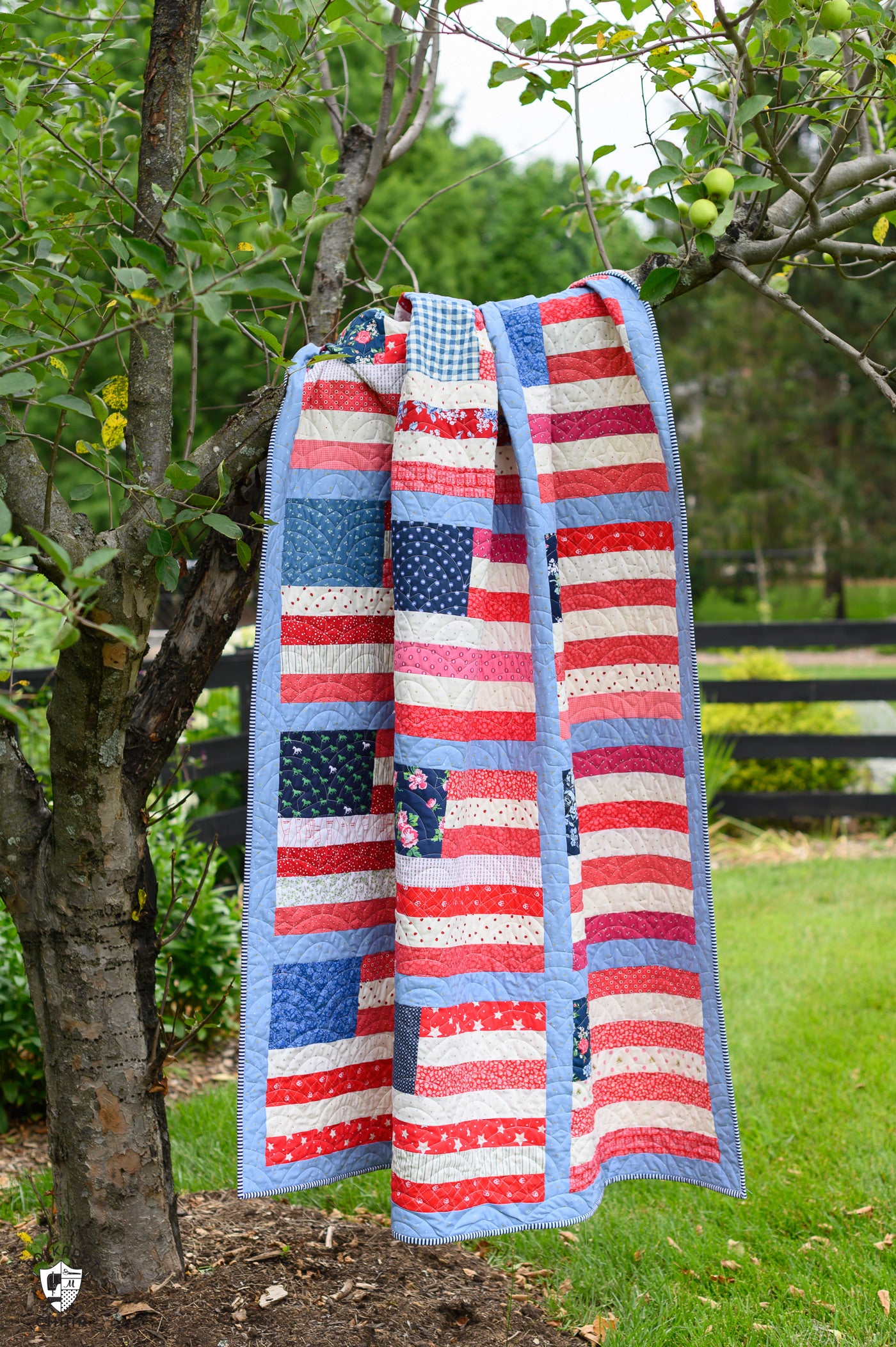 American flag-themed quilt draped over a tree branch outdoors