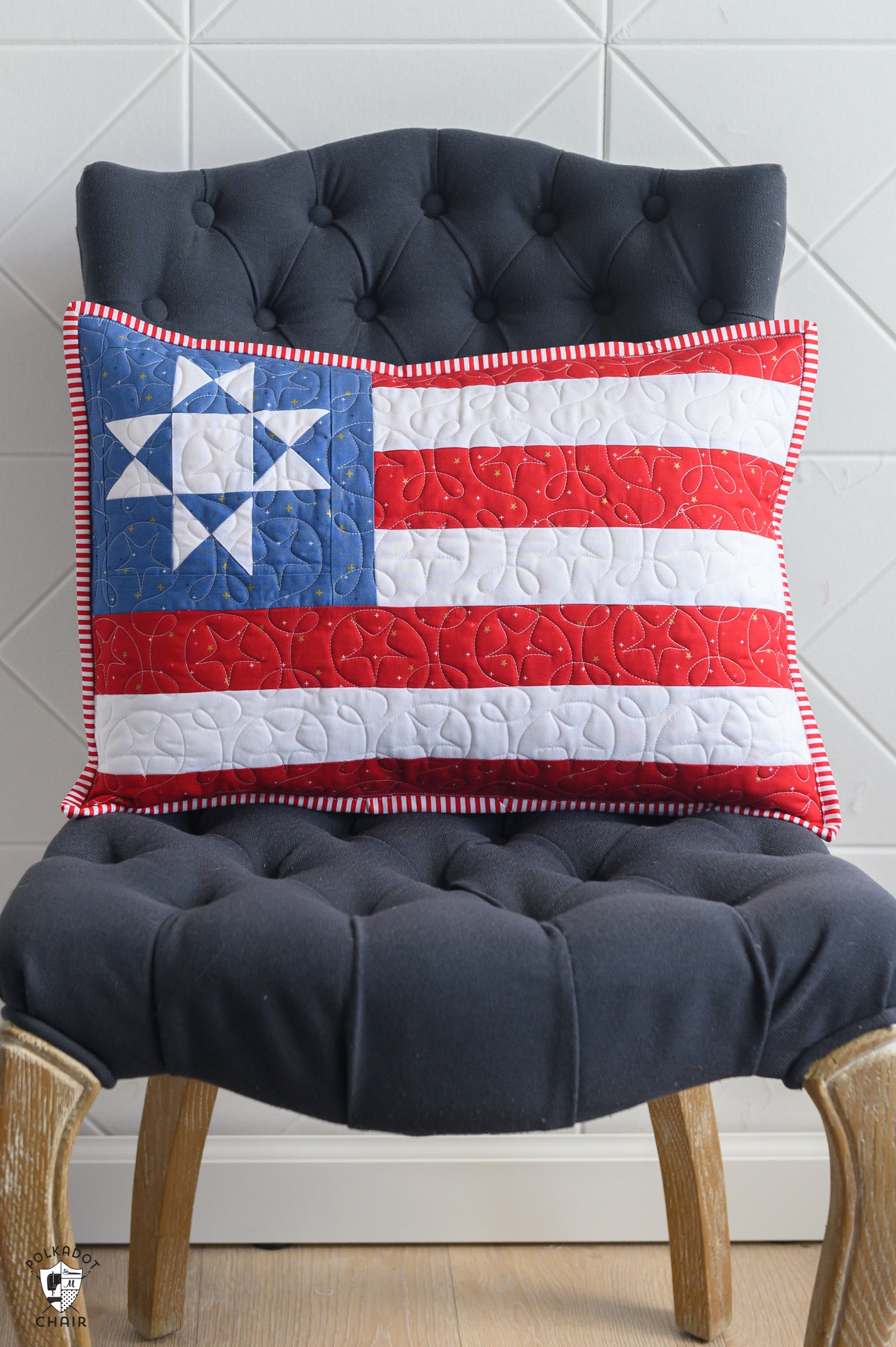 Quilted pillow with American flag design on a tufted chair against a white paneled wall.