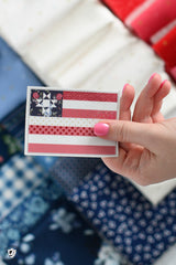 Hand holding a small quilt square with a star pattern against a fabric background